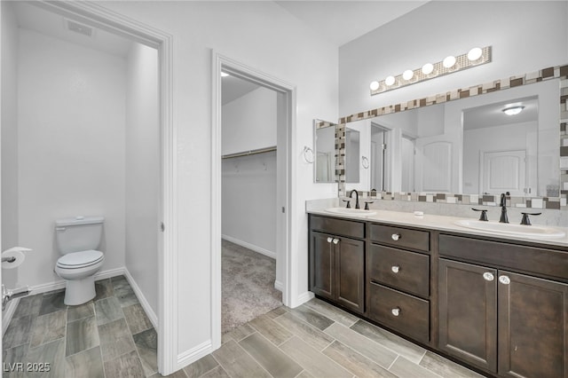 bathroom featuring a spacious closet, visible vents, toilet, and a sink