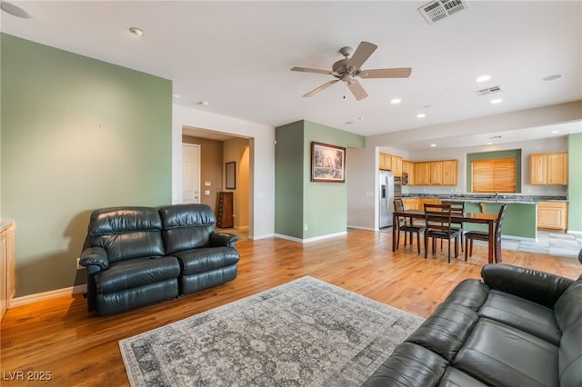 living room featuring baseboards, light wood-style floors, visible vents, and ceiling fan