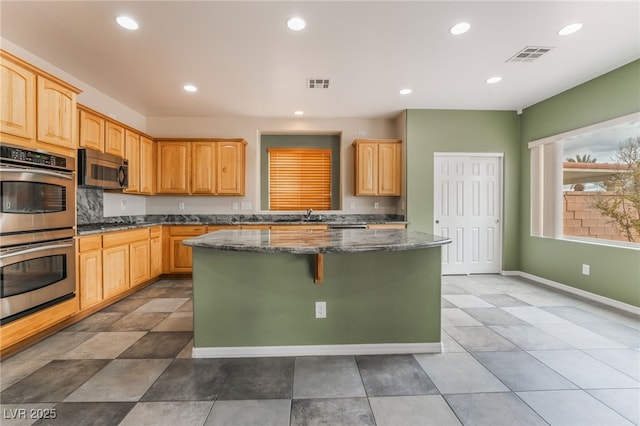 kitchen with a center island, visible vents, stainless steel appliances, and dark stone counters