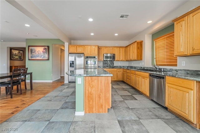 kitchen with dark stone countertops, visible vents, a sink, appliances with stainless steel finishes, and a center island