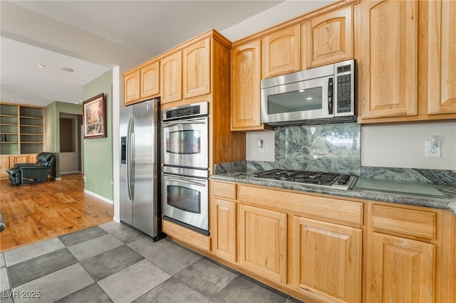 kitchen with light brown cabinetry, backsplash, stainless steel appliances, and baseboards