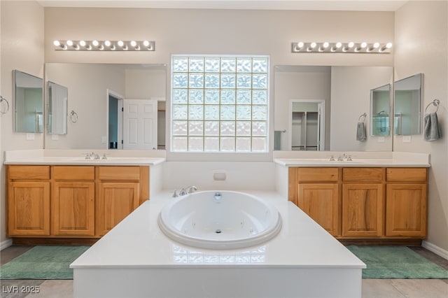 bathroom featuring tile patterned flooring, a tub with jets, a sink, and two vanities