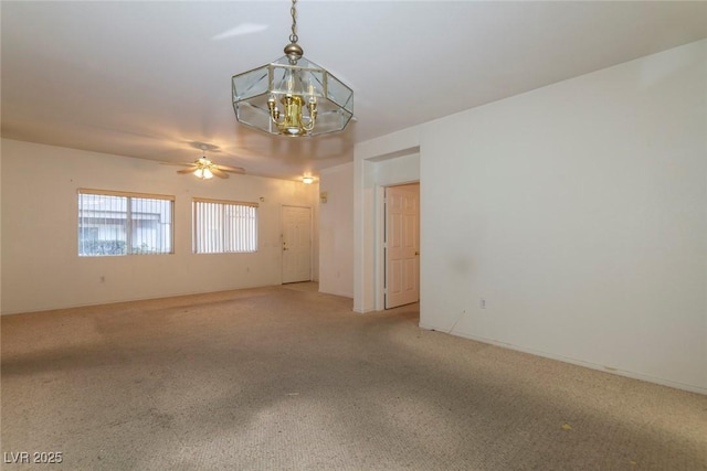 carpeted spare room featuring ceiling fan with notable chandelier