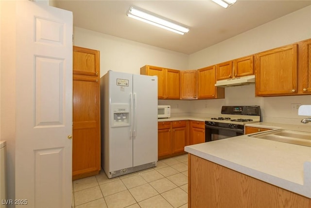 kitchen featuring under cabinet range hood, light countertops, light tile patterned floors, brown cabinets, and white appliances