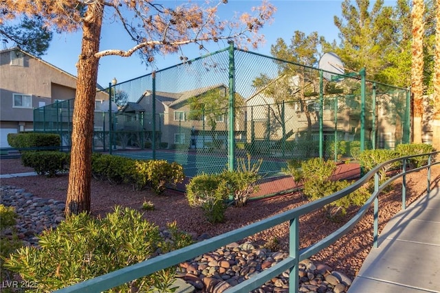 view of tennis court featuring community basketball court, fence, and a residential view