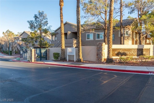 view of front of house with a residential view, stucco siding, a tiled roof, and a gate