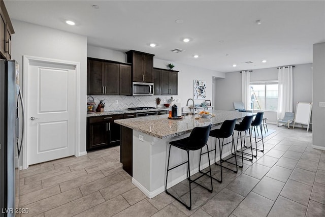 kitchen with a breakfast bar area, light stone countertops, visible vents, a kitchen island with sink, and stainless steel appliances