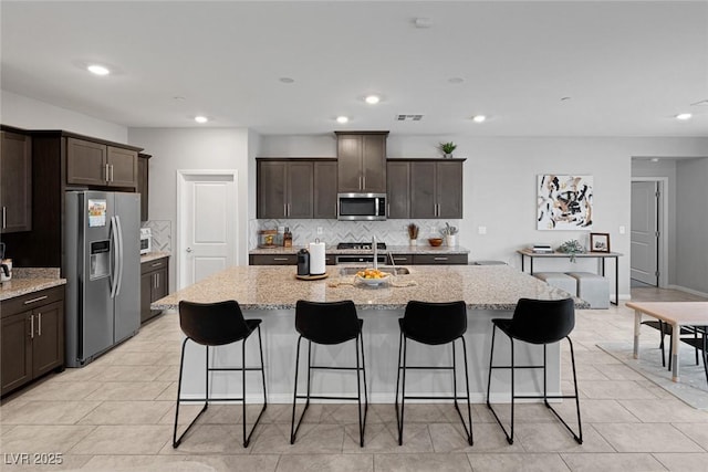 kitchen featuring dark brown cabinetry, light stone counters, tasteful backsplash, and stainless steel appliances