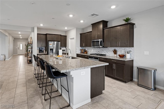 kitchen featuring visible vents, a sink, backsplash, stainless steel appliances, and dark brown cabinetry