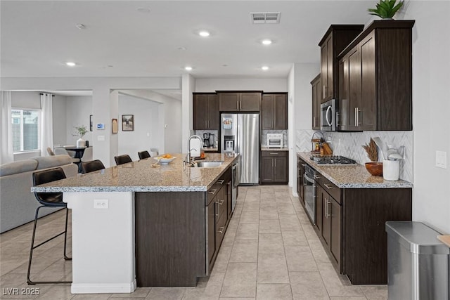 kitchen with visible vents, a sink, dark brown cabinetry, appliances with stainless steel finishes, and a kitchen breakfast bar