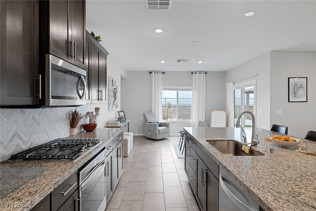 kitchen with decorative backsplash, appliances with stainless steel finishes, light stone countertops, and a sink