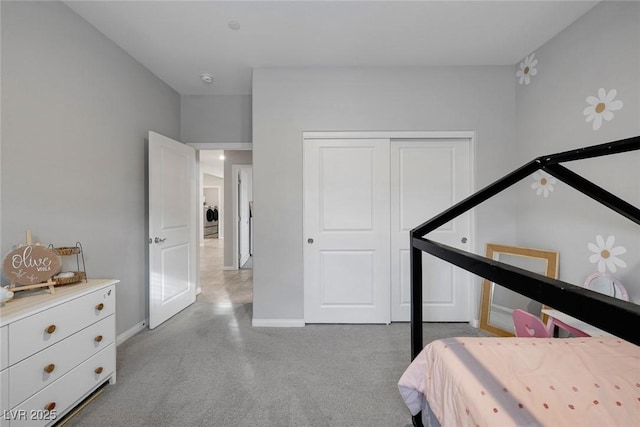 bedroom featuring a closet, baseboards, light colored carpet, and washer / dryer