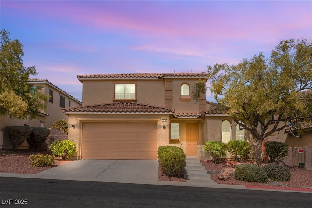 mediterranean / spanish house featuring stucco siding, a tiled roof, and concrete driveway