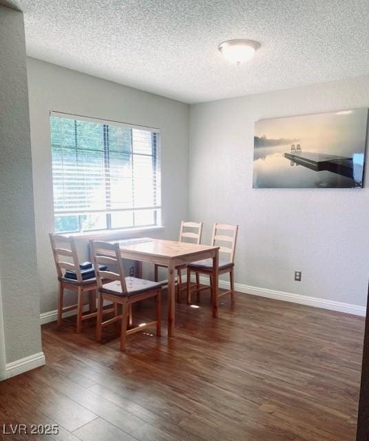 dining room featuring a textured wall, a textured ceiling, baseboards, and wood finished floors