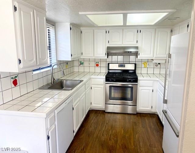 kitchen featuring under cabinet range hood, tile countertops, dark wood-style floors, white appliances, and a sink