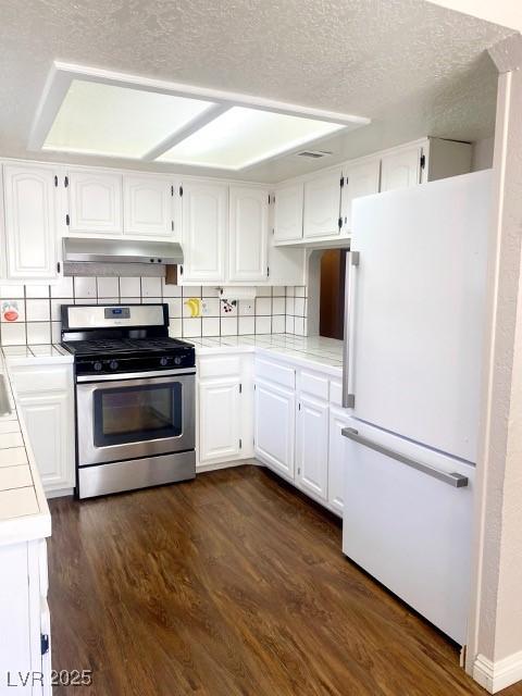 kitchen featuring under cabinet range hood, dark wood finished floors, freestanding refrigerator, white cabinets, and stainless steel gas range