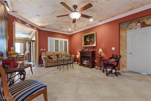 living room featuring crown molding, a ceiling fan, baseboards, and a warm lit fireplace