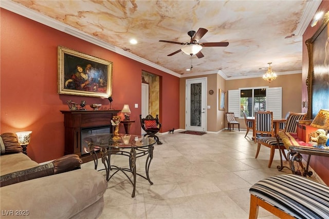 living area featuring baseboards, a glass covered fireplace, crown molding, and ceiling fan with notable chandelier