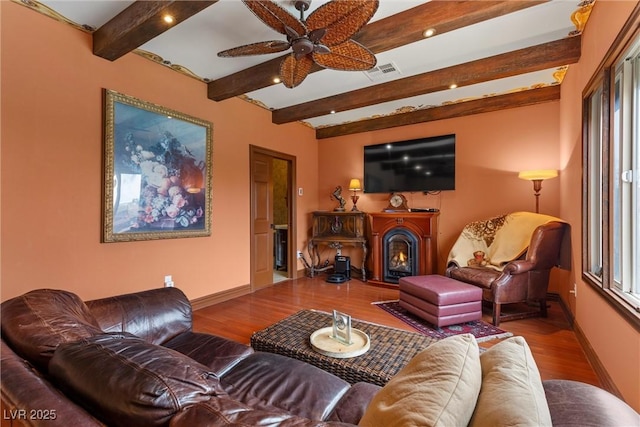 living area featuring visible vents, baseboards, a warm lit fireplace, and wood finished floors