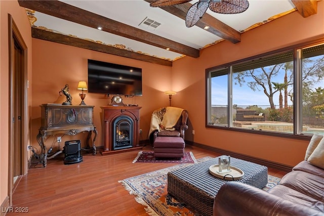 living room with wood finished floors, baseboards, visible vents, beam ceiling, and a lit fireplace