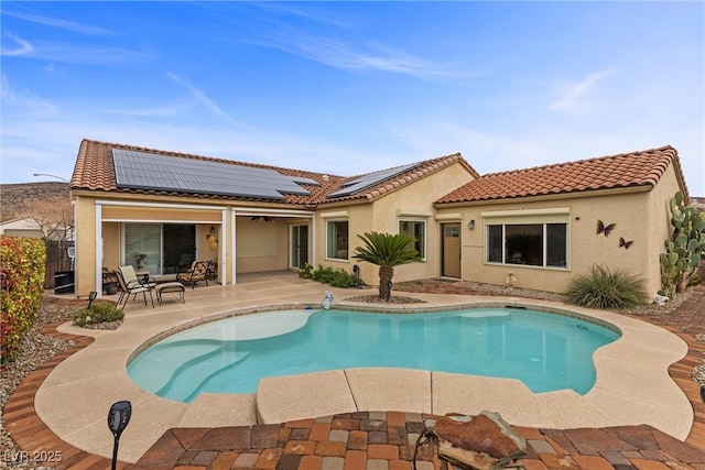 back of house with solar panels, an outdoor pool, stucco siding, a tiled roof, and a patio area