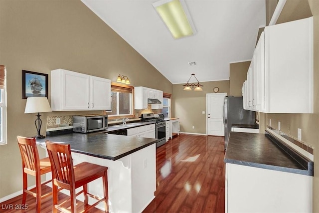 kitchen with a sink, stainless steel appliances, dark countertops, and a peninsula