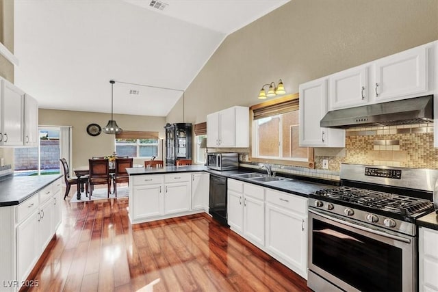 kitchen with dark countertops, under cabinet range hood, appliances with stainless steel finishes, a peninsula, and a sink