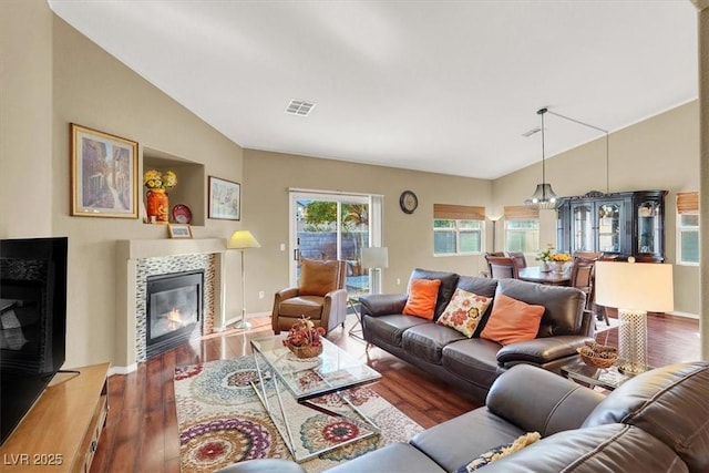 living area with a tile fireplace, wood finished floors, and vaulted ceiling