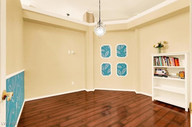 empty room featuring a chandelier, dark wood-type flooring, and baseboards