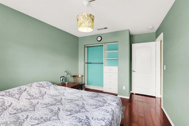 bedroom with wood finished floors, baseboards, visible vents, and a closet