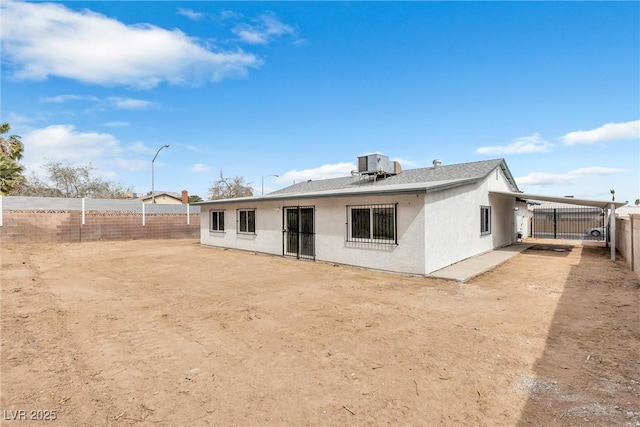 rear view of house featuring stucco siding, cooling unit, and a fenced backyard