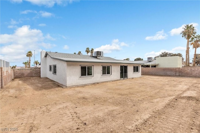 rear view of house with stucco siding, central AC unit, and a fenced backyard