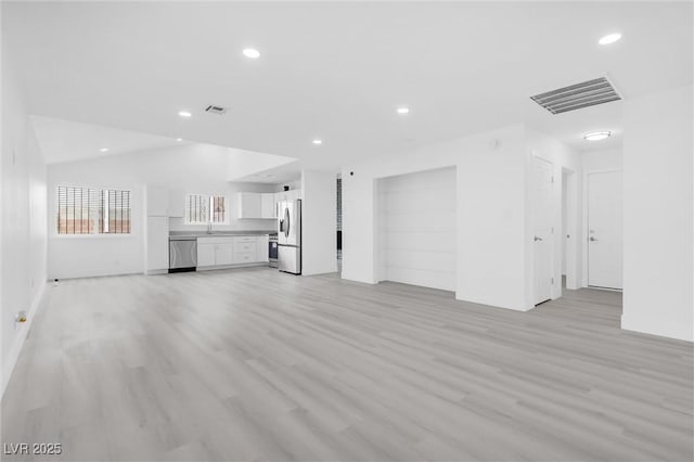 unfurnished living room with visible vents, light wood finished floors, lofted ceiling, recessed lighting, and a sink