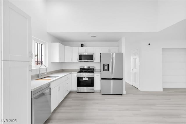 kitchen with light wood-type flooring, light countertops, appliances with stainless steel finishes, white cabinets, and a sink