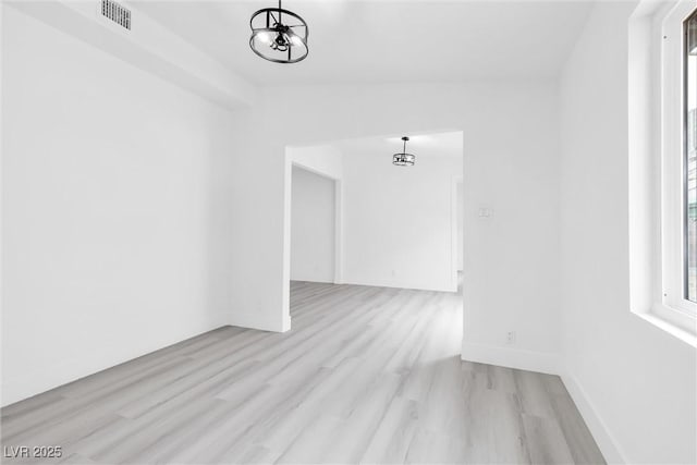 spare room with visible vents, wood finished floors, baseboards, a chandelier, and vaulted ceiling