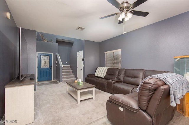 living room featuring visible vents, light carpet, ceiling fan, and stairway