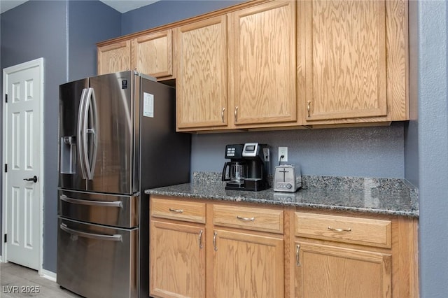 kitchen with dark stone countertops, light brown cabinets, and stainless steel refrigerator with ice dispenser