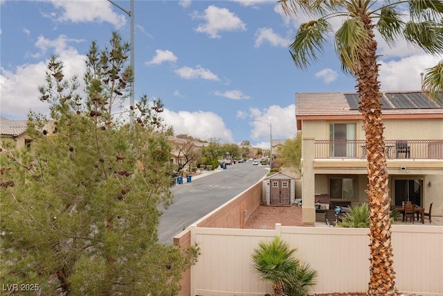 exterior space with stucco siding, a fenced front yard, roof mounted solar panels, an outdoor structure, and a balcony