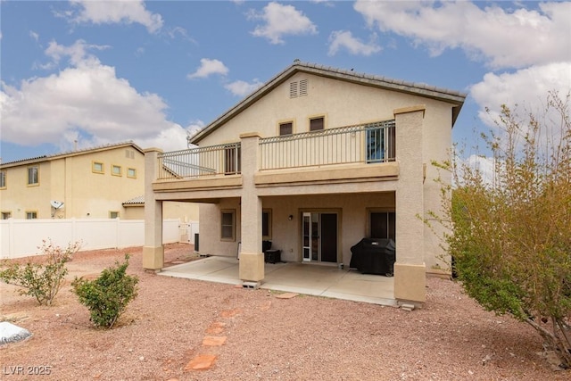 rear view of house with stucco siding, a balcony, a fenced backyard, and a patio area