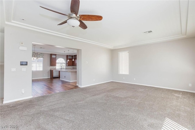 unfurnished living room with carpet, visible vents, baseboards, a raised ceiling, and ceiling fan with notable chandelier