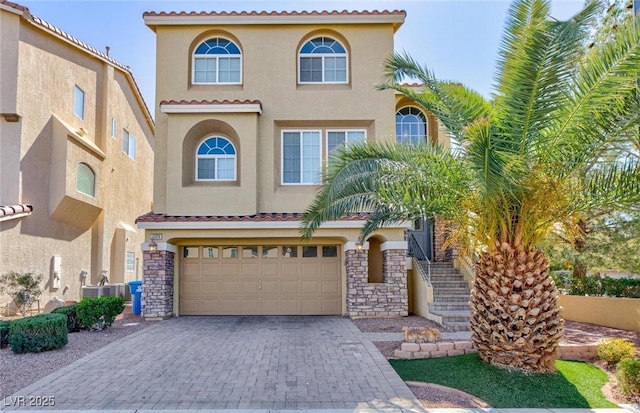 mediterranean / spanish house with stucco siding, decorative driveway, a garage, and a tiled roof