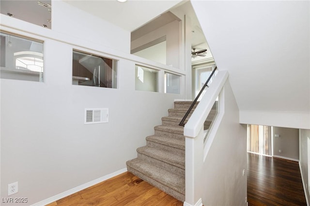 staircase featuring visible vents, baseboards, ceiling fan, and wood finished floors