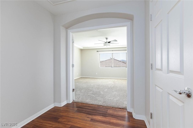 corridor featuring visible vents, baseboards, arched walkways, and dark wood-style floors