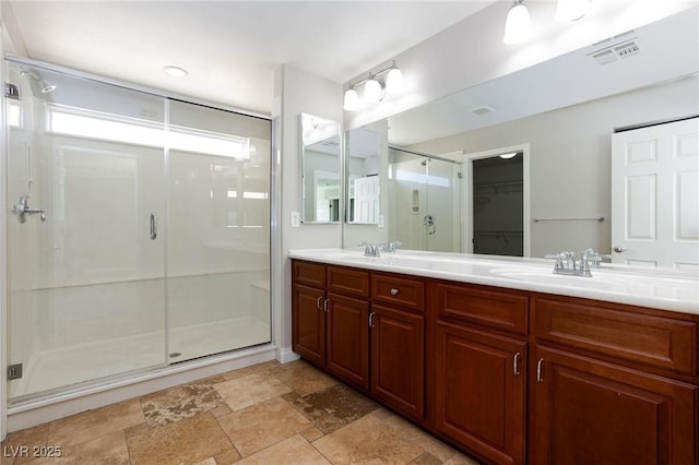 bathroom with a spacious closet, visible vents, a shower stall, double vanity, and stone finish floor