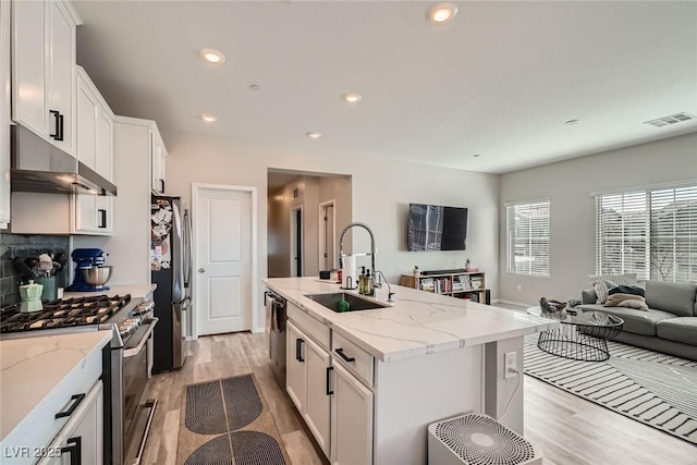 kitchen with visible vents, under cabinet range hood, open floor plan, appliances with stainless steel finishes, and a sink