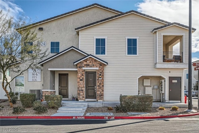 view of property with stone siding, stucco siding, central air condition unit, and a balcony