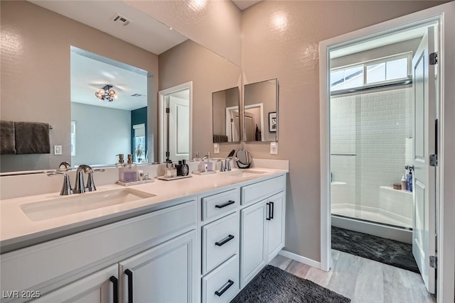 full bath with visible vents, a sink, a shower with door, wood finished floors, and double vanity