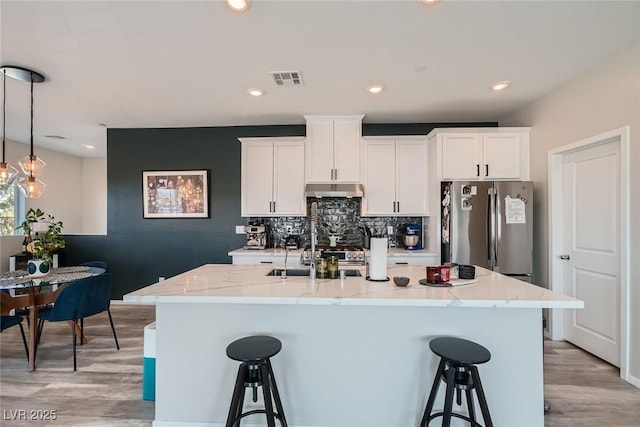 kitchen with under cabinet range hood, a breakfast bar, a sink, and freestanding refrigerator