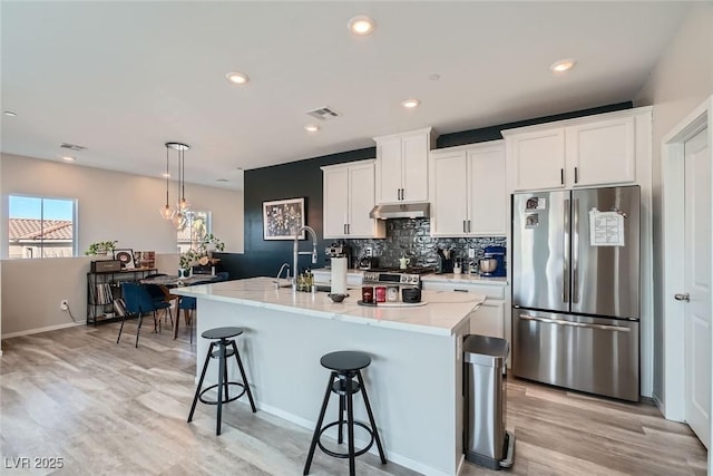 kitchen with a sink, under cabinet range hood, appliances with stainless steel finishes, a kitchen breakfast bar, and backsplash