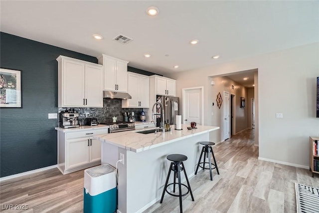 kitchen featuring visible vents, under cabinet range hood, a kitchen breakfast bar, stainless steel appliances, and a kitchen island with sink